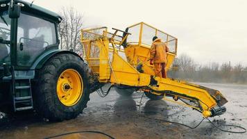 Washing of large-sized agricultural machinery. A worker in a yellow suit washes a tractor trailer. video