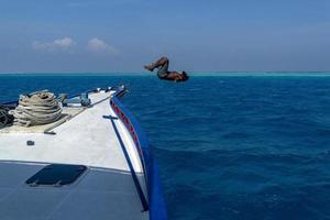 maldivo hombre saltando en agua y buceo desde barco foto