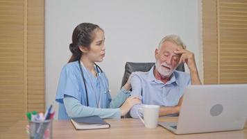 Caregiver checking on serious senior man during working with laptop at nursing home. Female talking to patient for resting from work video