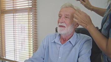 hembra asistente cepillado pelo de paciente mayor hombre. mujer Ayudar abuelo para Corte de pelo a hogar. video