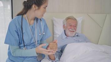 vrouw verzorger Holding hand- geven ondersteuning en empathie naar glimlachen senior Mens Aan bed. gelukkig opa ontspannende en voorbereidingen treffen naar slaap video