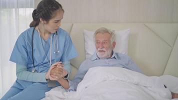 asiatico femmina badante Tenere anziano uomo mano dando supporto e empatia. donna assunzione cura di paziente su letto nel assistenza infermieristica casa. assistenza sanitaria e medico assicurazione concetto