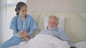 hembra cuidador participación mano dando apoyo y empatía a sonriente mayor hombre en cama. contento abuelo relajante y preparando a dormir video