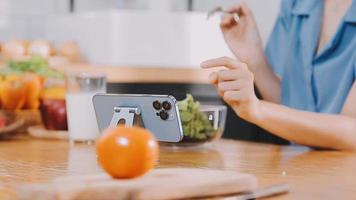 Professional beautiful happy young woman is blogging for her kitchen channel about healthy living in the kitchen of her home and looking on camera on a tripod video