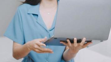 efficiente giovane del Millennio ragazza seduta su un' letto nel il mattina, usi il computer portatile computer e mangia Cornetti e bevande caffè per prima colazione. superiore giù sparo. video