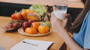 Professional beautiful happy young woman is blogging for her kitchen channel about healthy living in the kitchen of her home and looking on camera on a tripod video