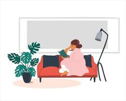 A young woman reads a book while sitting under a blanket on a red sofa in the apartment. vector