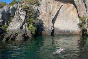 turista nadando en genial lago taupo con maorí rock tallas el icónico turista atracción sitio en lago taupo, nuevo zelanda foto