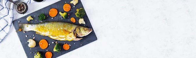 Baked sea bass fish with vegetables and greens on stone plate photo