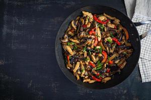 Stir fry with chicken, eggplant and pepper in wok pan on dark background photo