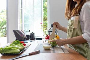 young woman is making salad from vegetables she has prepared on table in her home kitchen to get salad that is clean and safe because ingredients are carefully selected. healthy food preparation ideas photo