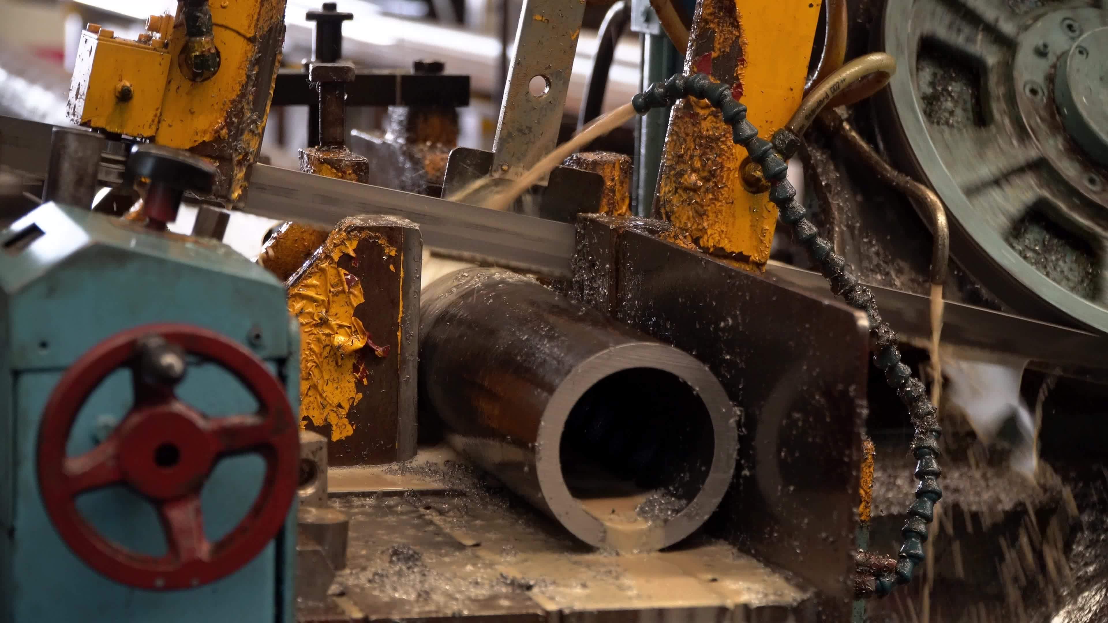 Industrial band saw, cutting metal pipe, coolant in yellow scene
