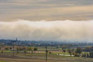 huge wall of white fog over a village with fields photo