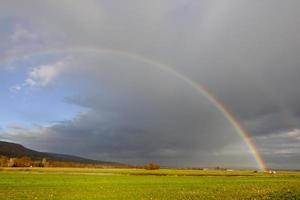 rainbow on dark rain clouds over green fields in the winter photo