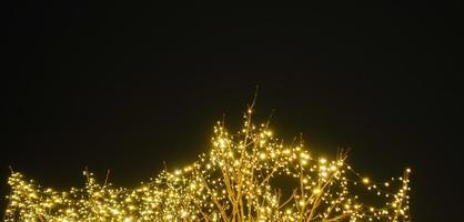 árbol con muchos brillante luces a un Navidad mercado con negro cielo en el antecedentes panorama foto