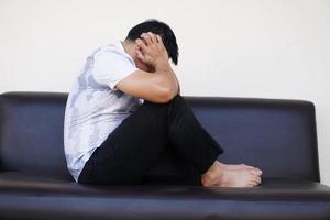 Depressed man sits alone on sofa, feeling sad, anxious , cry, covered his ears, don't want to know or listen to anything. Concept, mental health  problems, depression. photo