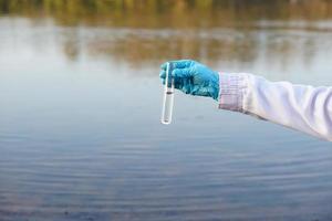 Closeup researcher hands wears blue gloves holds test glass tube that contain sample water from the lake. Concept, explore, inspect quality of water from natural source. photo