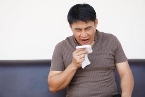 asiático hombre capturas un frío, estornudos, sostiene pañuelo de papel papel. concepto, salud problemas, alergia síntomas , estornudar ,tos, líquido nariz. foto