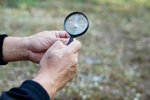 Closeup hand hold magnify glass to explore tiny grass flowers.   Concept, examine, explore, research nature or biological organisms. Study about environment and plants. Science tool photo