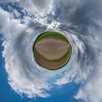 tiny planet in blue overcast evening sky with beautiful clouds with transformation of spherical panorama 360 degrees. Spherical abstract aerial view. Curvature of space. photo