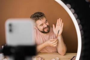 Man talking on cosmetics holding a makeup tools while recording his video. Guy making video for his blog on cosmetic product photo