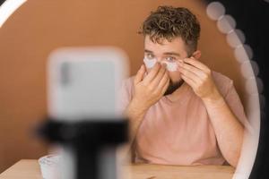 Man vlogging about make up and beauty products. Male shooting a makeup tutorial. Guy teaching make up tutorial using her phone - diversity and blogger concept. photo