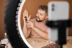 Man vlogging about make up and beauty products. Male shooting a makeup tutorial. Guy teaching make up tutorial using her phone - diversity and blogger concept. photo