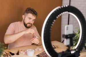 Portrait bearded man making vlog review cosmetics product and channel recording video make up tutorial making at home - Online influencer guy and social media market live steaming concept photo