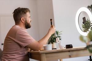 Man vlogging about make up and beauty products. Male shooting a makeup tutorial. Guy teaching make up tutorial using her phone - diversity and blogger concept. photo