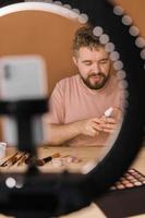 Man recording video vlog while applying cosmetics or explore cosmetic product. Guy making tutorial make-up for his blog on cosmetics. photo
