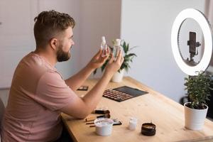 Man recording video vlog while applying cosmetics or explore cosmetic product. Guy making tutorial make-up for his blog on cosmetics. photo