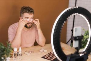 Man vlogging about make up and beauty products. Male shooting a makeup tutorial. Guy teaching make up tutorial using her phone - diversity and blogger concept. photo