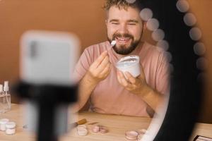 Man vlogging about make up and beauty products. Male shooting a makeup tutorial. Guy teaching make up tutorial using her phone - diversity and blogger concept. photo