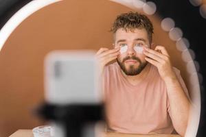 Man recording video vlog while applying cosmetics or explore cosmetic product. Guy making tutorial make-up for his blog on cosmetics. photo