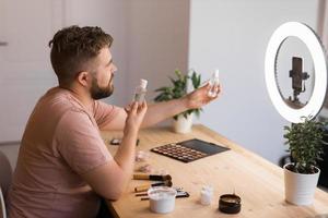 Man vlogging about make up and beauty products. Male shooting a makeup tutorial. Guy teaching make up tutorial using her phone - diversity and blogger concept. photo