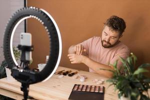 Man recording video vlog while applying cosmetics or explore cosmetic product. Guy making tutorial make-up for his blog on cosmetics. photo