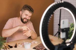 hombre vlogging acerca de hacer arriba y belleza productos masculino disparo un maquillaje tutorial. chico enseñando hacer arriba tutorial utilizando su teléfono - diversidad y blogger concepto. foto
