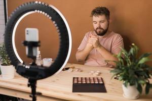 Man vlogging about make up and beauty products. Male shooting a makeup tutorial. Guy teaching make up tutorial using her phone - diversity and blogger concept. photo