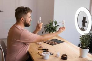 Man vlogging about make up and beauty products. Male shooting a makeup tutorial. Guy teaching make up tutorial using her phone - diversity and blogger concept. photo