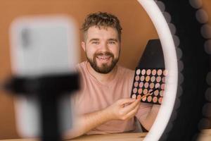 Male beauty blogger doing his make up and recording a video lesson his with mobile phone - vlog, diversity and video blog concept photo