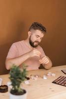 Portrait of happy man beauty blogger sitting in room at table and speaking recommending foundation or decorative cosmetic looking at camera. Blogging and vlog concept photo