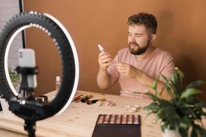 Man recording video vlog while applying cosmetics or explore cosmetic product. Guy making tutorial make-up for his blog on cosmetics. photo