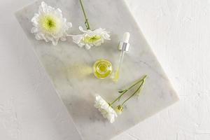 top view of an open cosmetic bottle with serum or oil for face and body care. marble white podium and flowers. natural cosmetics. photo