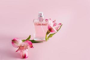 a bottle of perfume or cosmetic spray on a pink background with astromeria flowers. the concept of advertising a natural fragrance. a copy space. photo