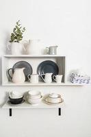 various cookware on open white shelves on a white stylish wall. vertical view. decorative items in the interior of the kitchen. photo