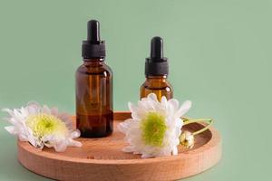 two bottles with a dropper with a natural remedy or serum for organic skin care of the face stand on a wooden plate. front view. green background. photo