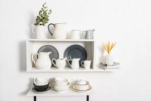 many different jugs under water and milk are on the kitchen open shelves. bowls and plates. Beautiful white interior view of the kitchen shelves. photo