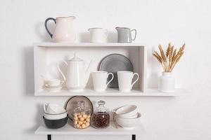 foreground view, close-up of open kitchen shelves with porcelain and ceramic utensils. stylish kitchen background in white tones. photo