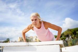 Senior woman working strength training push ups against sky with copyspace. photo