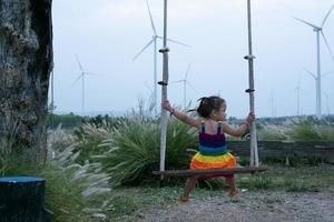 hermosa joven madre hija relajante sentado verano prado antecedentes y viento turbinas, viento turbinas como un alternativa energía fuente, el concepto de sostenible recursos. foto